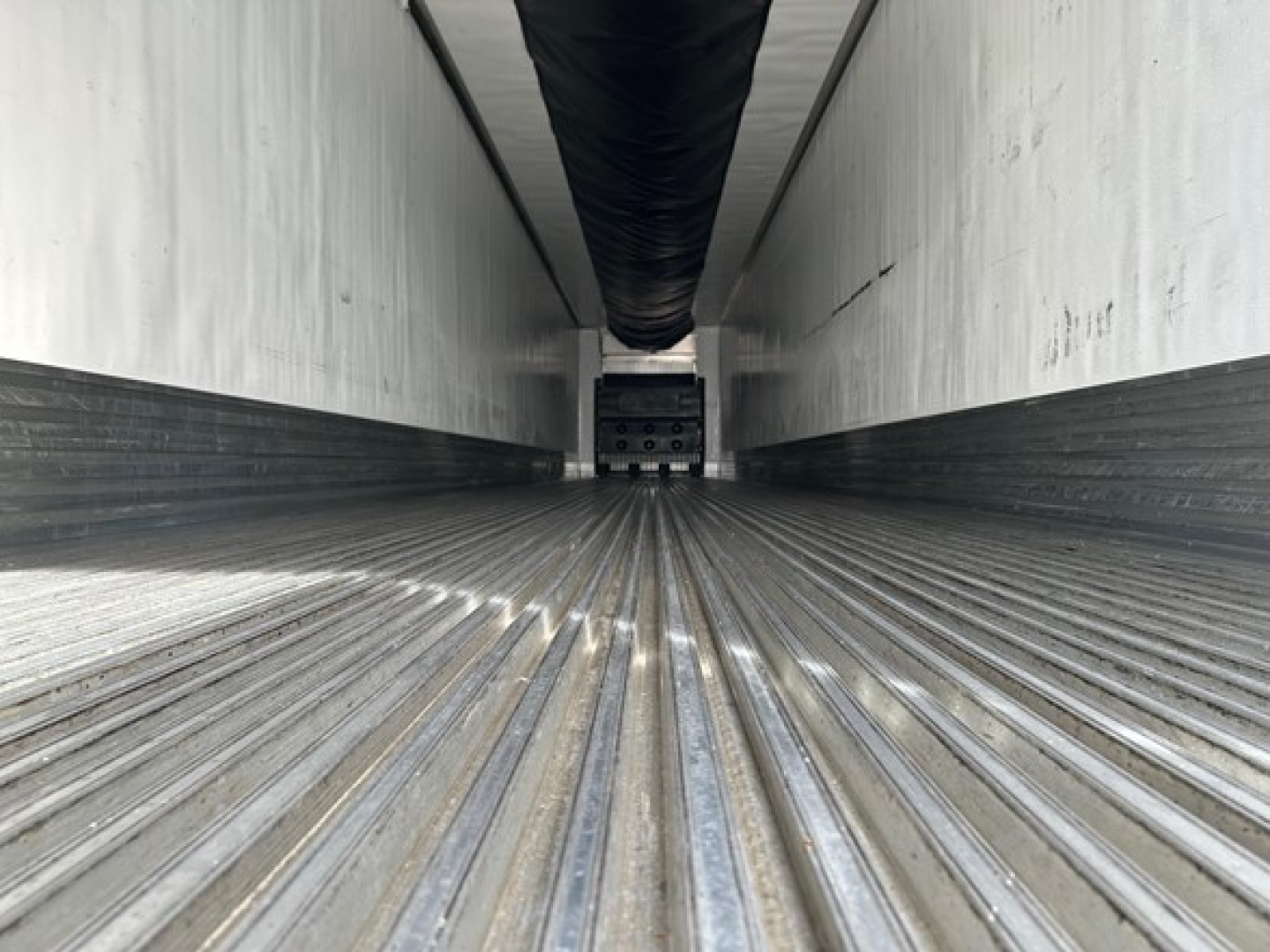 Trailer interior with ribbed metal floor, nose-to-back view showing ceiling ducts and side walls; empty cargo space of a reefer trailer.