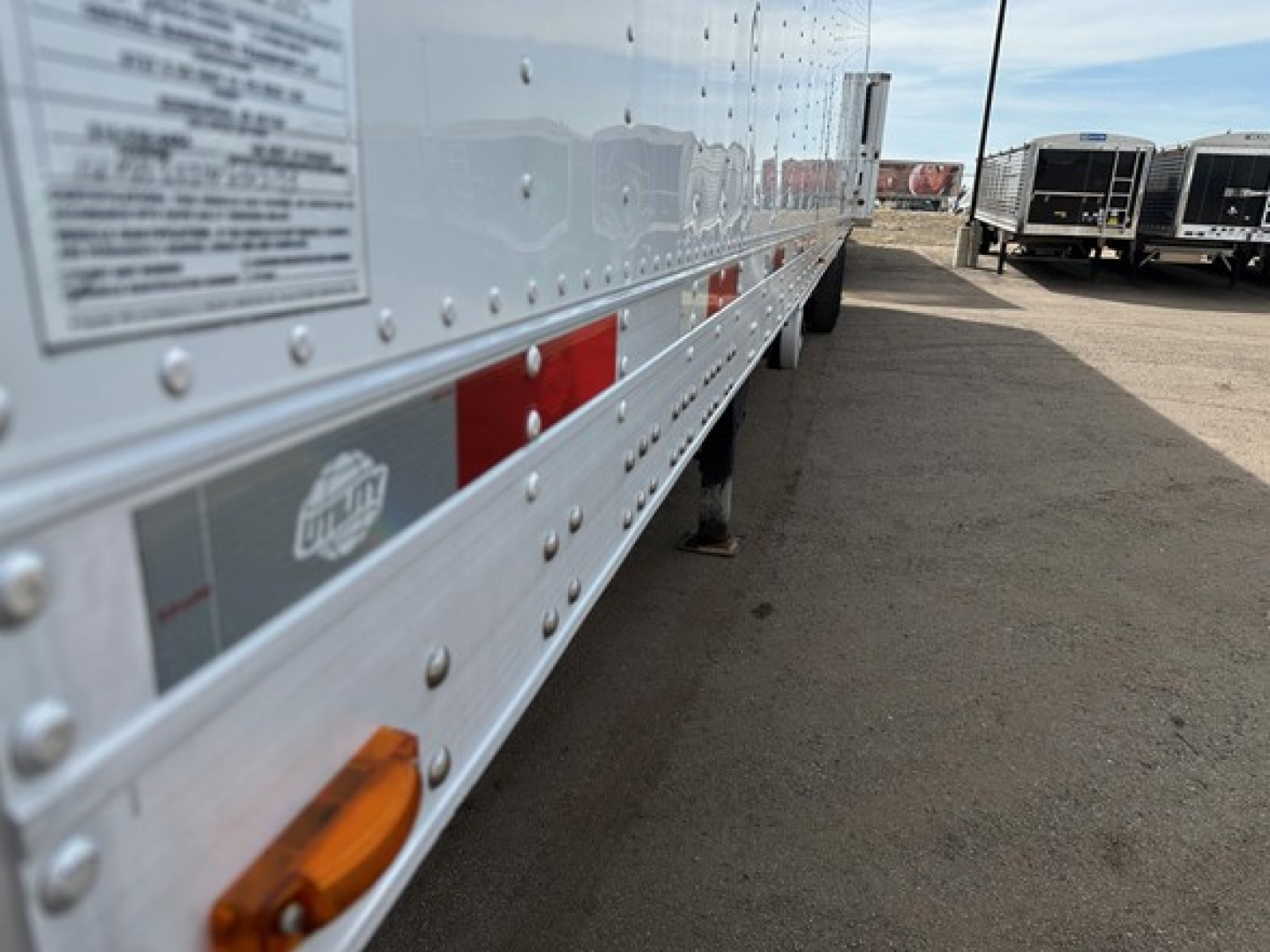 Trailer side of a 2022 Utility 3000R reefer trailer showing riveted aluminum body, reflectors, and small inspection sticker along the lower rail.