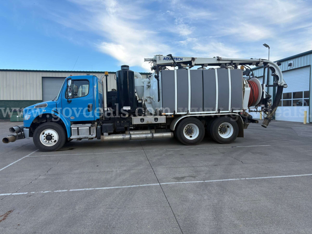 Freightliner M2 106 vacuum truck side view showing large gray vacuum tank, hoses, and crane equipment on bed.