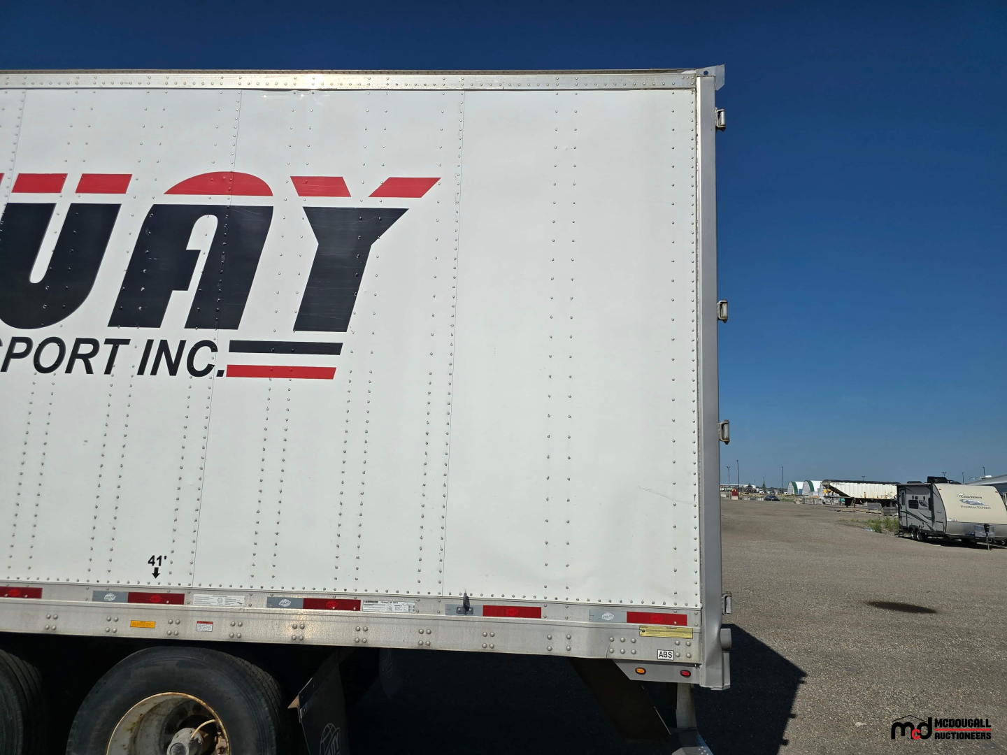 Utility trailer side showing large 'US' or 'U' lettering on white box with tandem axle at a truck yard.