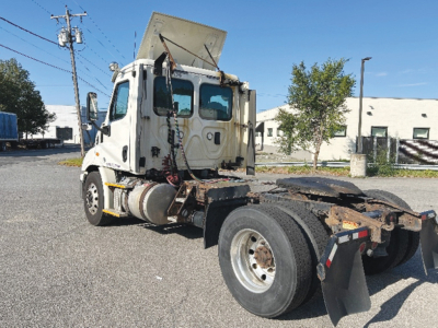 Truck cab and chassis of a Freightliner Cascadia 113 from a side/rear view. Front of cab with raised sleeper and exposed engine bay area. Visible tires, fifth wheel plate, and mudflaps.