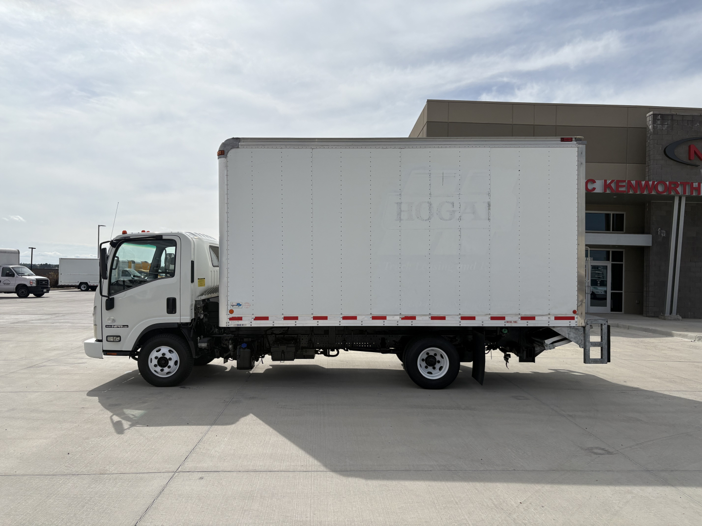 Isuzu NPR-HD box truck in side profile view with plain white cargo box and cab, dealership building in background.