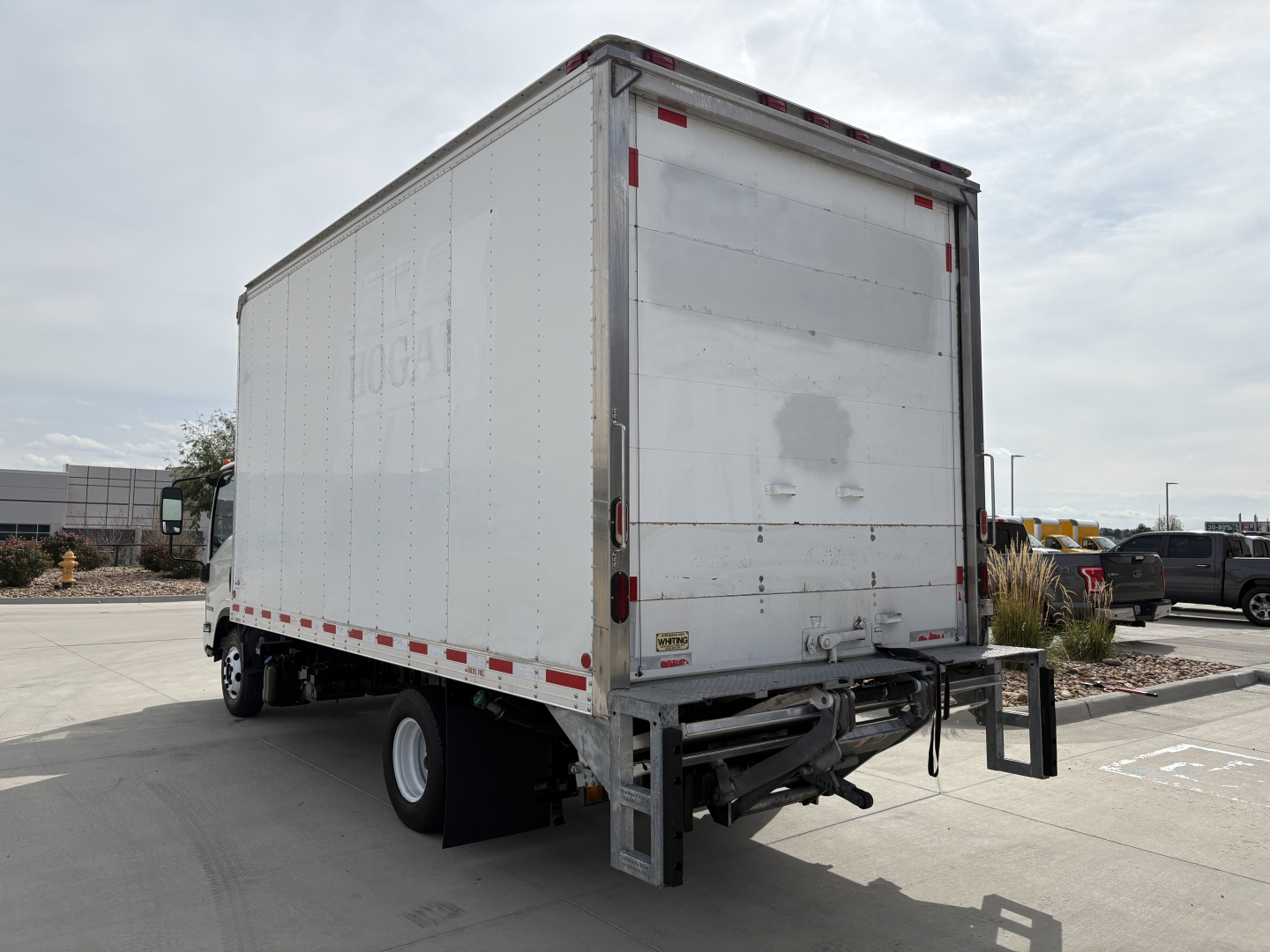 Isuzu NPR-HD box truck rear view showing large white cargo box with empty doors and rear bumper, black hitch area, and reflective safety tape.