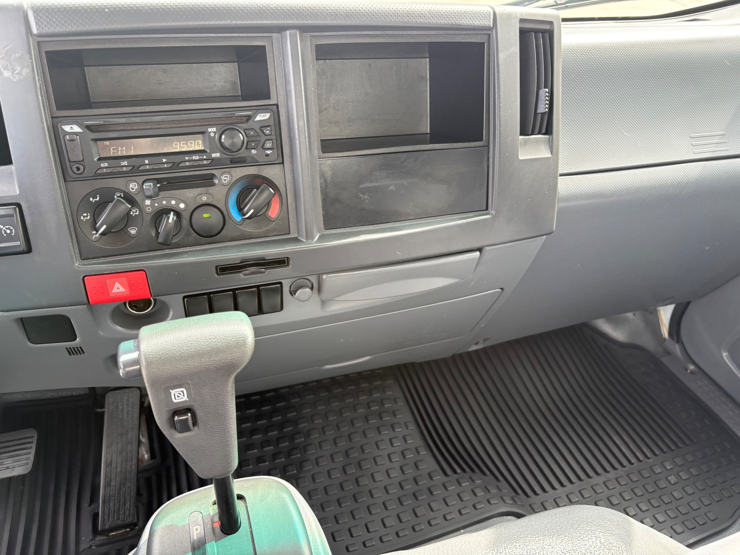 Isuzu NPR-HD cabin dash with gear shifter, center console, climate controls, and empty storage compartments.