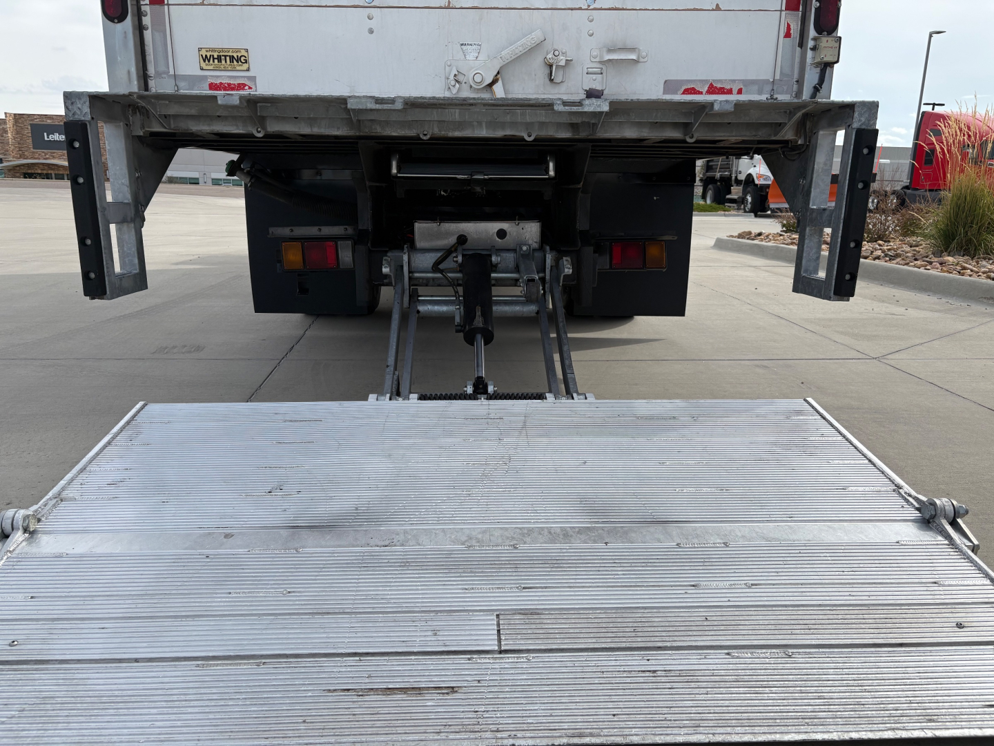 Isuzu NPR-HD rear view showing lift or ramp mechanism and metal platform at tail with hitch and surrounding chassis components.