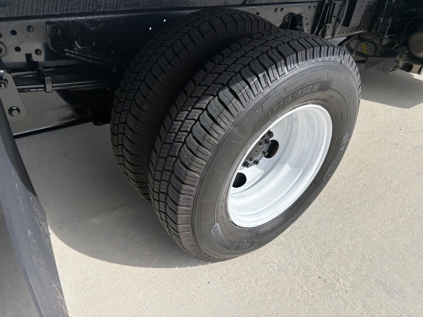 Isuzu NPR-HD chassis with front wheel and tire showing wheel cap; portion of truck frame and black underbody visible.