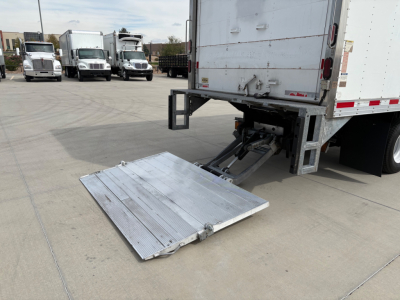 Truck rear with hydraulic lift gate in lowered position and aluminum platform, Isuzu NPR-HD box truck in background.
