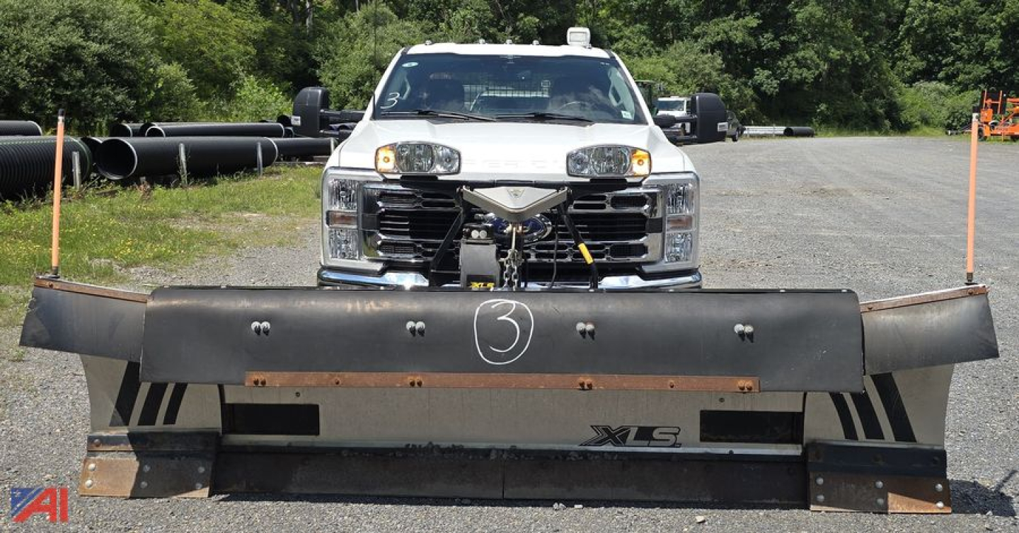 Front view of a white 2023 Ford F-350 Super Duty with a large snow plow attachment. Plow shows XLS branding and mounting hardware; truck headlights and grille visible.