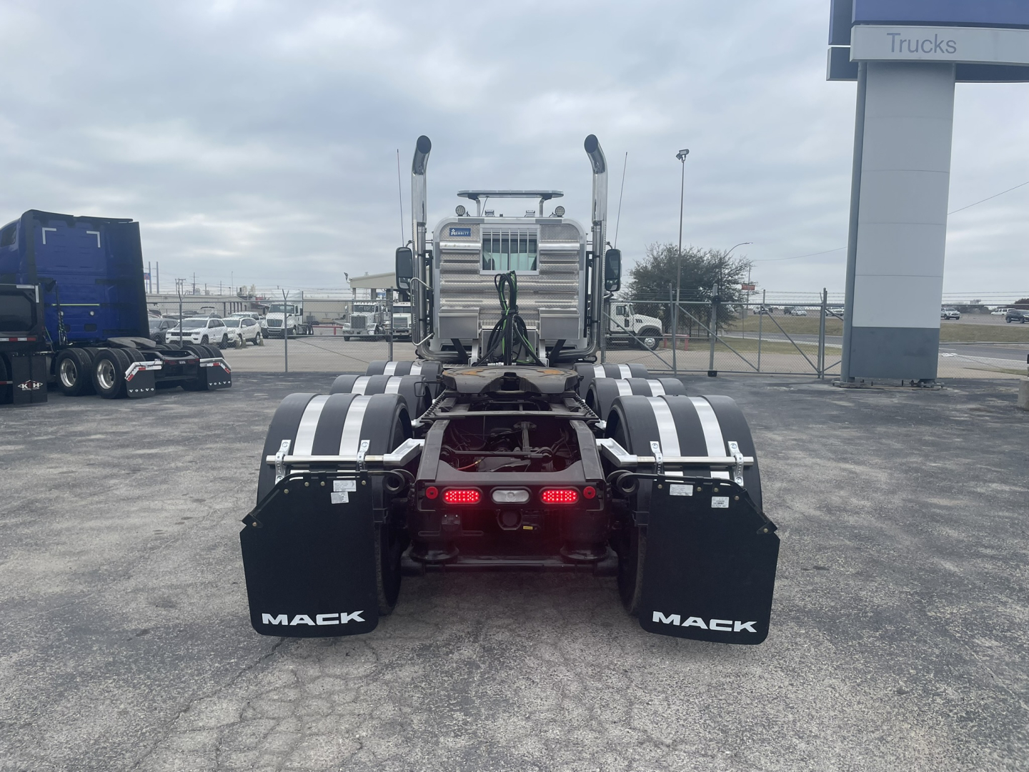 Mack GR84FT truck rear view showing dual rear axles, mud flaps with ‘MACK’, and red taillights in a dealership lot.
