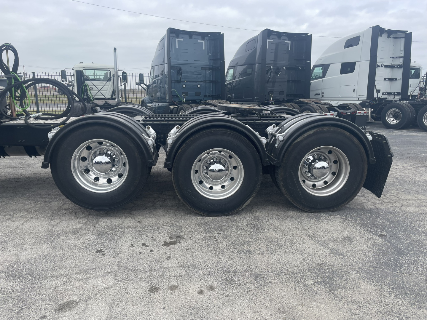 Three-axle tractor rear wheels and mudflaps of a new Mack GR84FT truck chassis with other cab units in the background.
