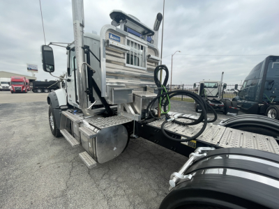 Mack GR84FT cab area with aluminum steps and access ladder, fuel tanks, and attached hoses; front grille visible, tag areas and chrome components.