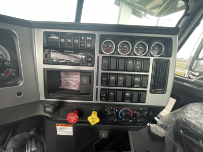 Truck cab instrument cluster and dashboard showing gear selector indicators, auxiliary gauges, switches, and climate controls in a Mack GR84FT cab.