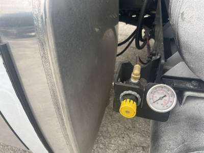 Mack GR84FT engine bay area showing air gauge with yellow knob and valve, mounted near a metal surface and hoses.