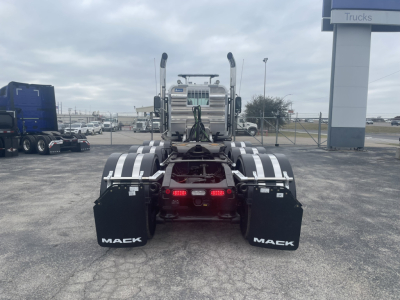 Mack GR84FT truck rear view showing dual rear axles, mud flaps with ‘MACK’, and red taillights in a dealership lot.