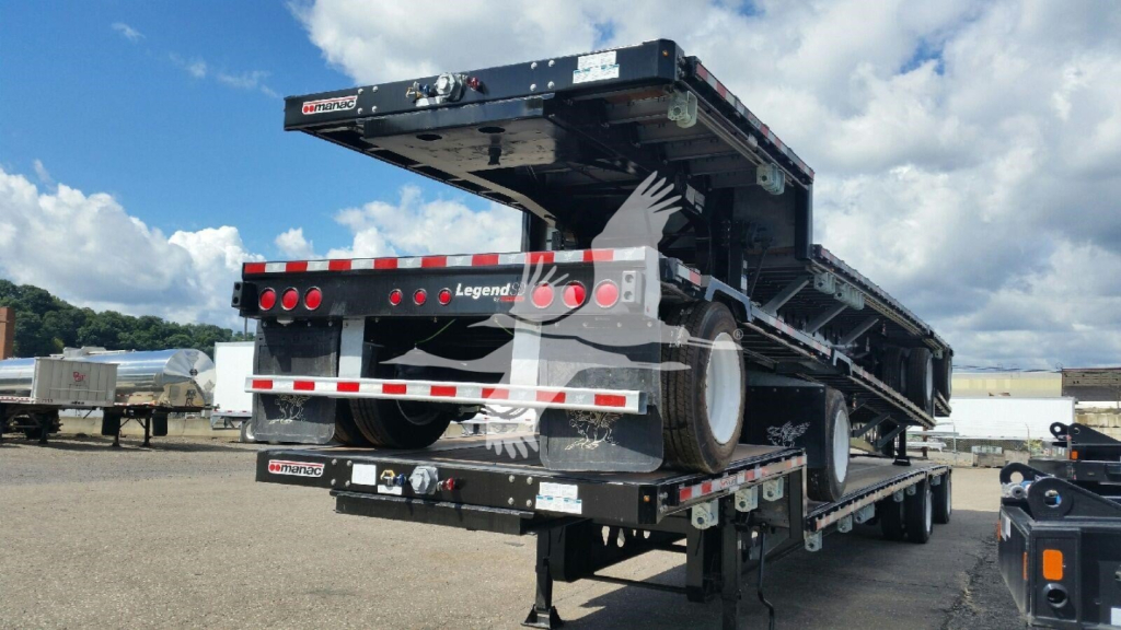 Manac dropdeck trailer rear/side view showing stacked deck, black with red/white reflective tape; rear bumper, taillights, and undercarriage visible.