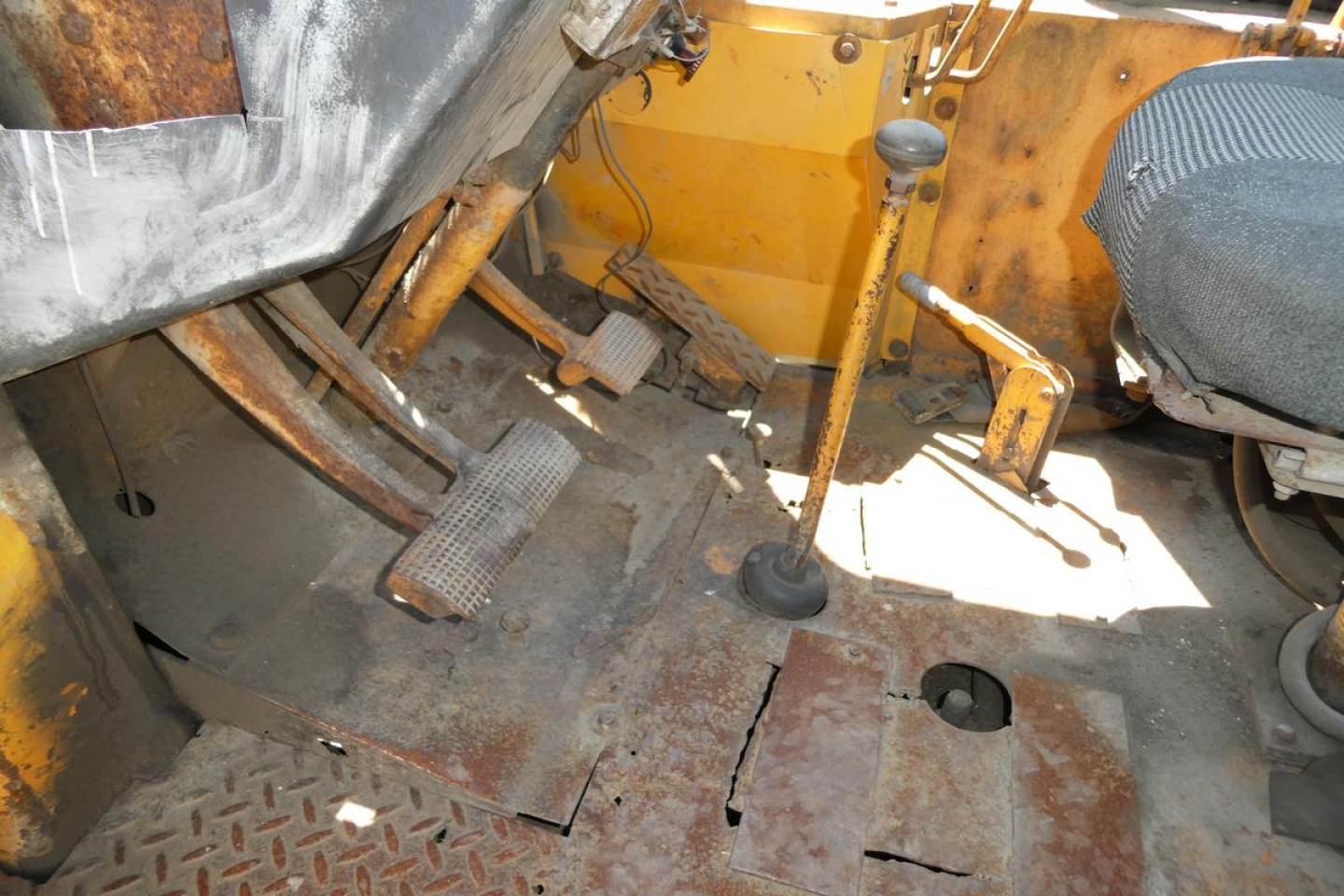Loader cab interior showing pedals and floor with rust patina and exposed metal floor plates