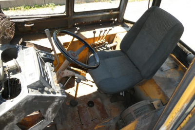 Cab interior of a 1979 Case 480C loader showing steering wheel, array of levers, and operator seat with rugged metal floor and dusty surfaces.