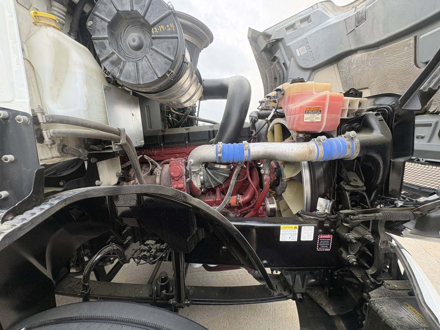 Mack AN42T engine bay showing cooling system hoses, coolant reservoir, air intake, and engine block with red paint accents.