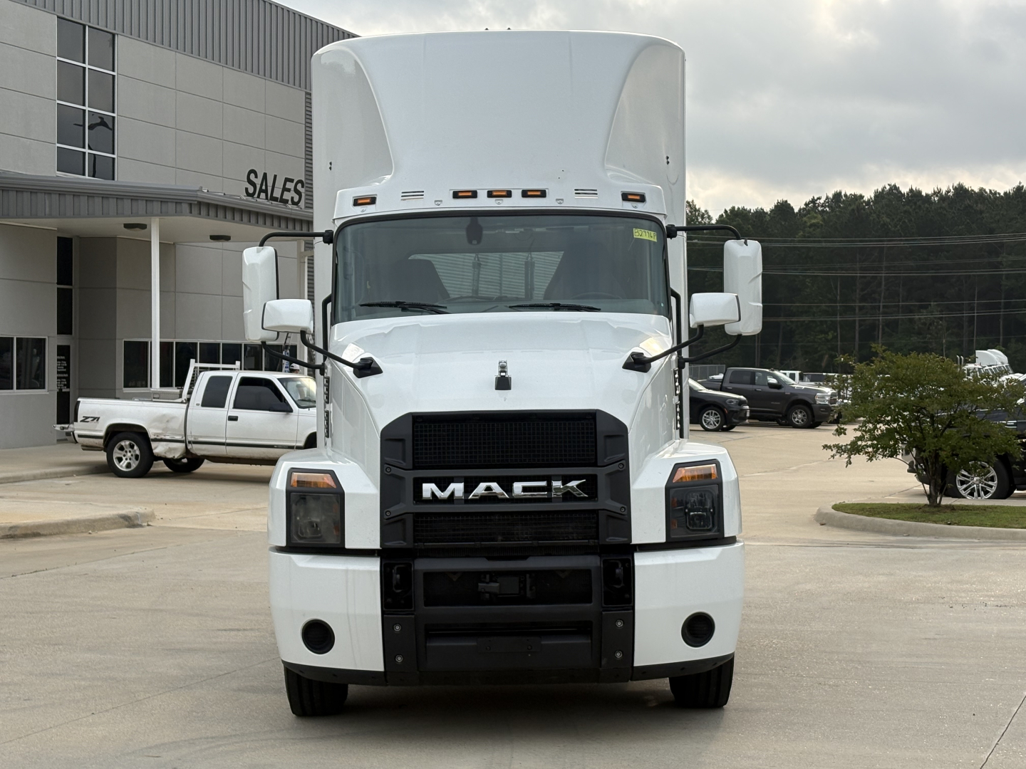Front view of a white Mack AN42T daycab truck showing grille with MACK logo and large bumper, in a dealership lot.