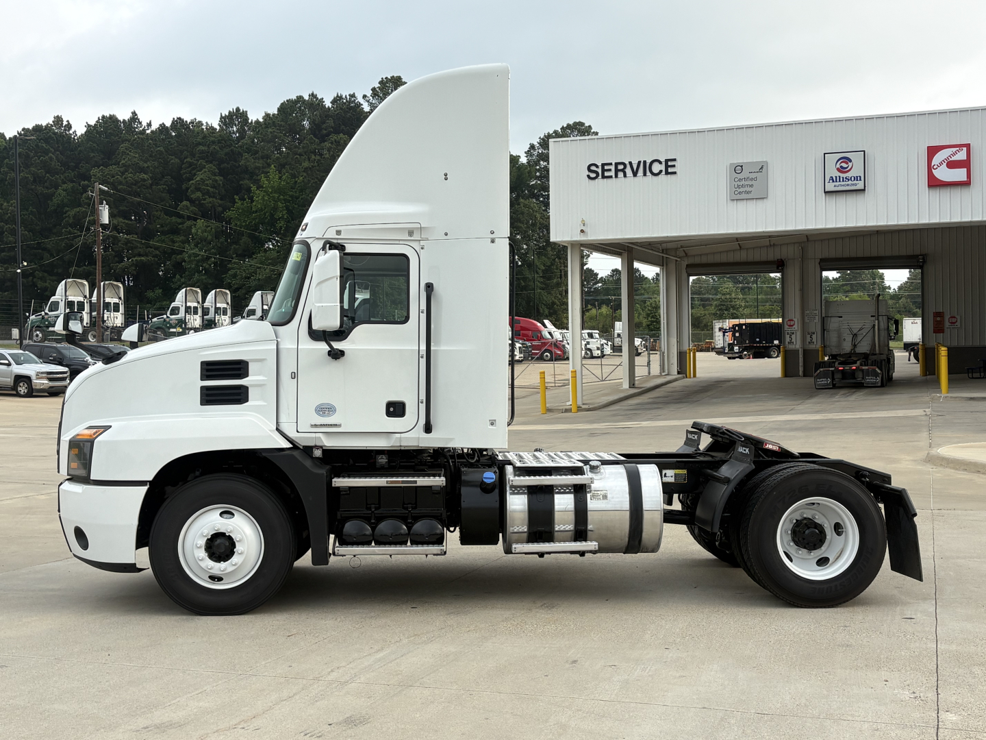 Truck cab and chassis of a 2022 Mack AN42T Daycab showing fuel tanks and side view with service building in background.