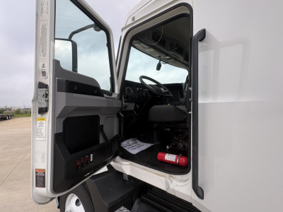 Truck cab interior with open door showing steering wheel and dashboard; fire extinguisher mounted near floor; gray interior panels; window and mirror visible.