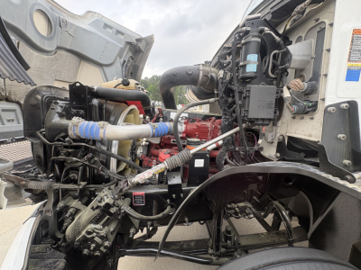 Mack AN42T truck engine bay showing diesel engine components, hoses, and wiring; view includes turbo hoses, coolant reservoir, and air intake area.