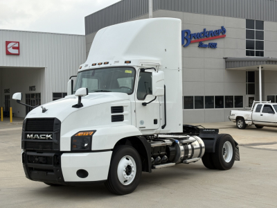 Mack AN42T tractor cab parked in front of dealership building, white exterior, aerodynamic sleeper top, front grille with MACK lettering, visible fuel tanks and rear wheels.