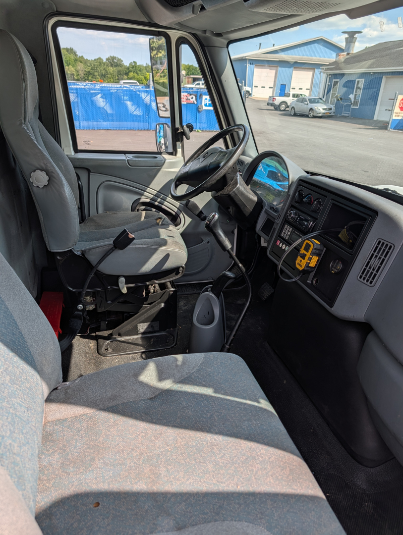Truck cab interior of a 2006 International 4300 showing driver's seat, steering wheel, dashboard with gauges, and gray fabric upholstery.