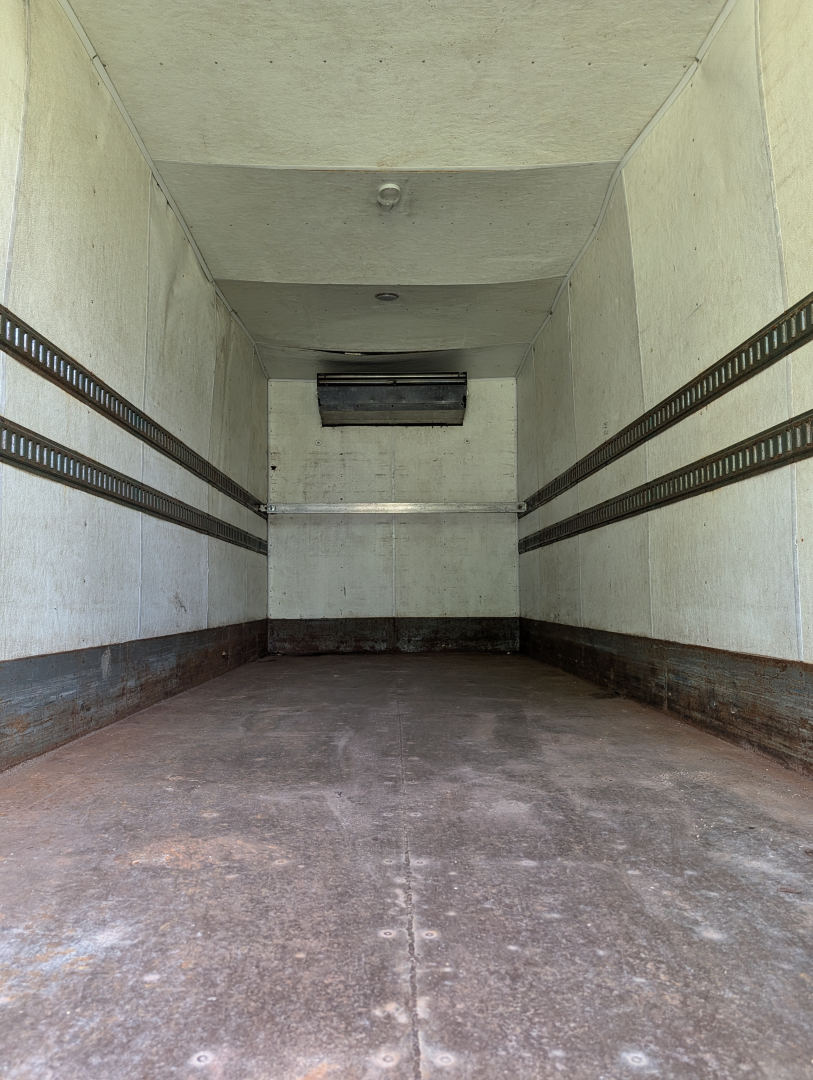 Interior view of an empty cargo box trailer showing white walls with horizontal E-track rails, a raised ceiling, and a small vent at the far end.