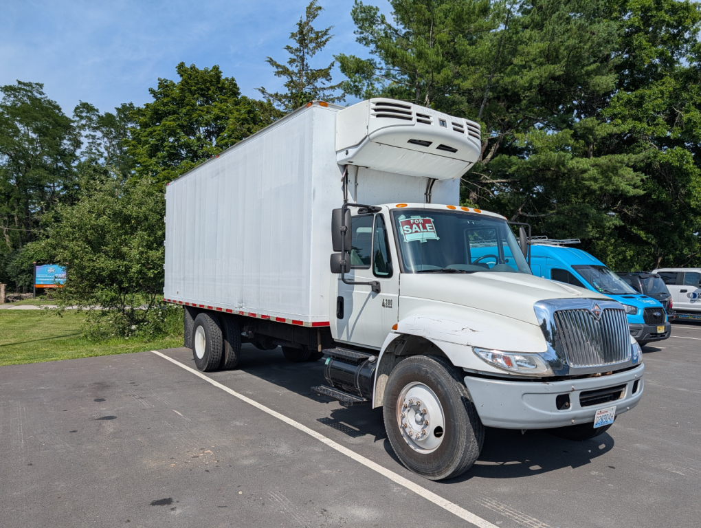 Box truck with a large white refrigerated box on a modern International cab and chassis, for sale in a parking lot.