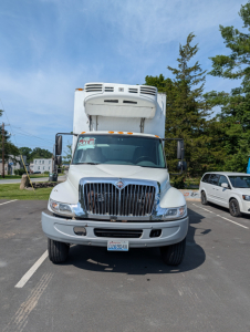 Front view of a white 2006 International 4300 box truck with a large grille and raised refrigerated box, showing sale sign in windshield.