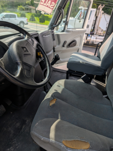 Interior of a 2006 International 4300 box truck showing steering wheel, dashboard, and front seats with wear on the driver's seat.