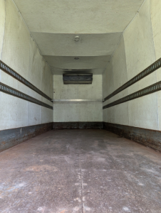 Interior view of an empty cargo box trailer showing white walls with horizontal E-track rails, a raised ceiling, and a small vent at the far end.