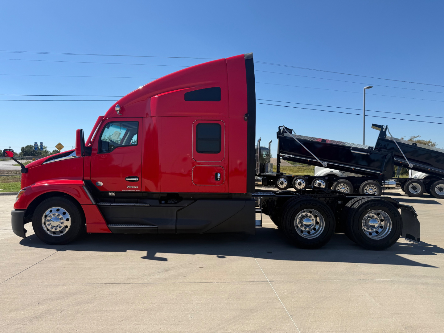 Kenworth T680CON conventional sleeper truck in red with a dump trailer attached, side view showing cab and dual rear axles.