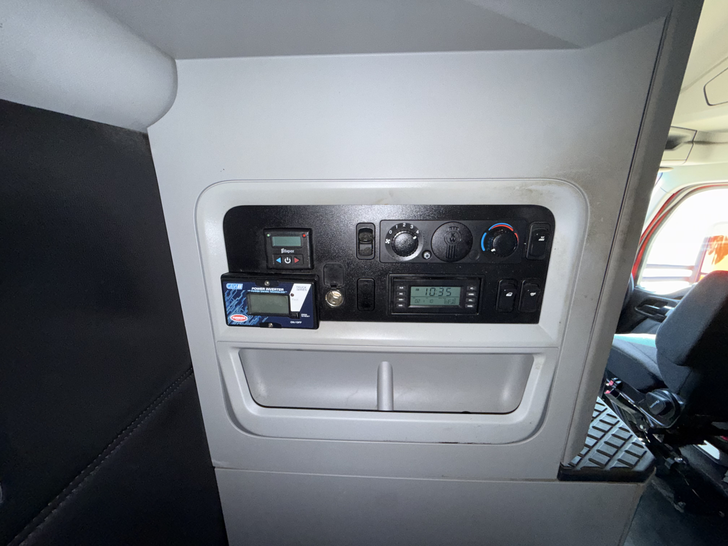 Dashboard panel in Kenworth T680 showing control switches, circular dials, and a small digital display. Includes a blue card reader slot and various gauges.