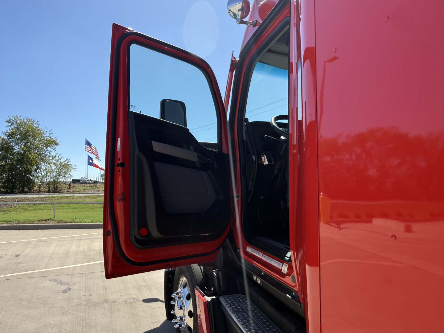 Truck door open on a red Kenworth T680 cab showing interior door panel and entry step.