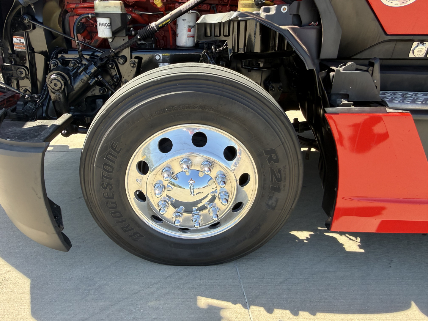 Kenworth T680 front wheel area showing large Bridgestone tire with polished chrome hub and red fender.