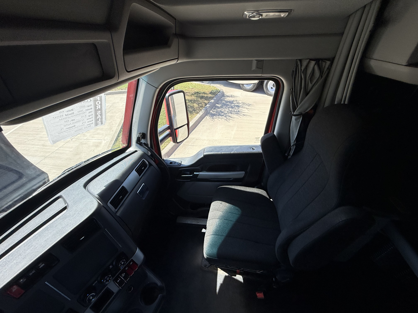 Kenworth T680 truck interior view of the driver’s seat and dashboard from the cab doorway, with steering wheel, controls, and side window visible.