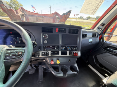 Cab interior of a 2023 Kenworth T680 showing dashboard with steering wheel, digital gauge cluster, center console, climate controls, and cup holders.