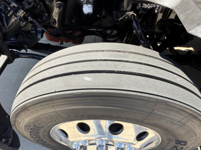 Kenworth T680 front wheel area showing front tire and axle assembly with exposed suspension components under the cab.