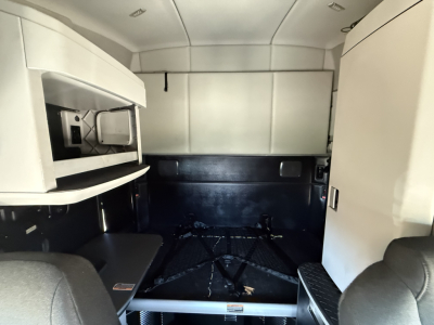 Kenworth T680 sleeper tractor cab interior showing sleeping area and storage compartments with light gray walls and black floor.