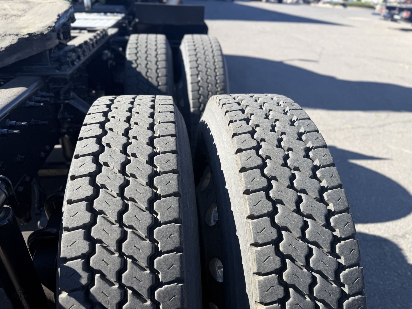 Dual rear truck tires on a Mack Anthem tractor trailer with visible tread pattern and chassis components.