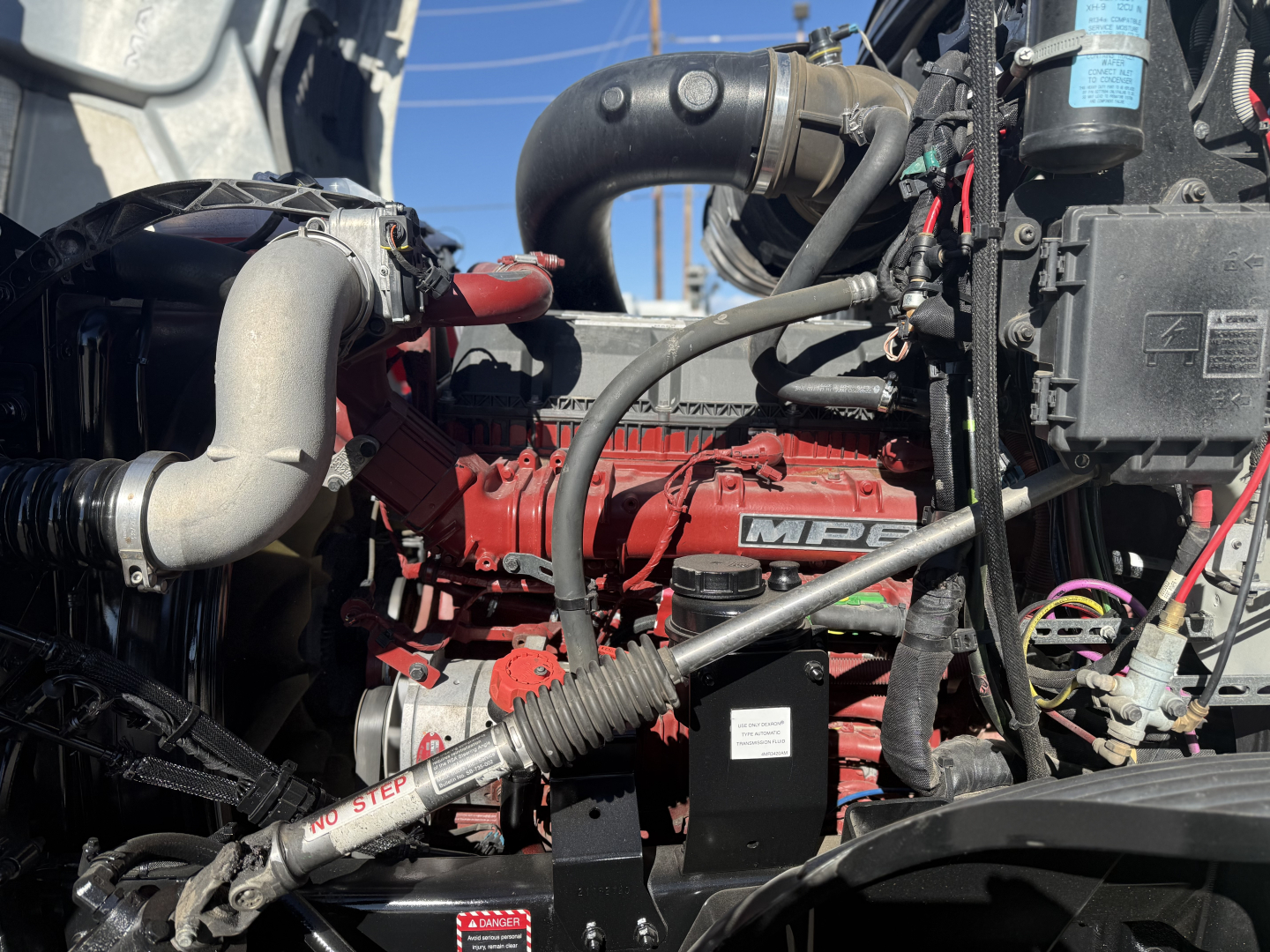 Mack ANTHEM truck engine bay showing red MPI engine with intake piping, wiring, hoses, and auxiliary components.