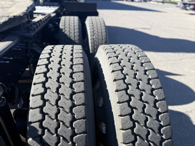 Dual rear truck tires on a Mack Anthem tractor trailer with visible tread pattern and chassis components.