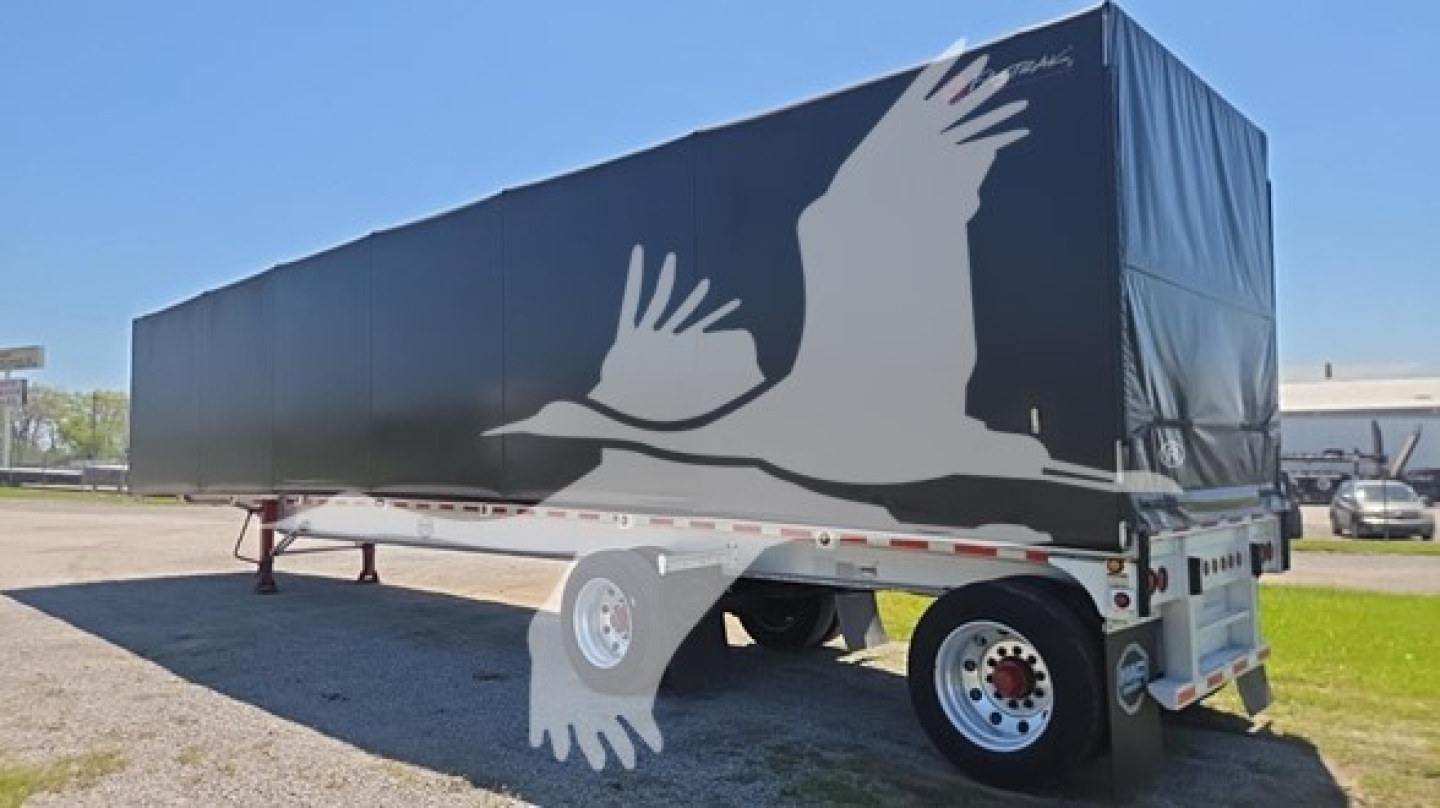 Trailer side view showing curtainside trailer with large white dove graphic on dark blue tarpaulin and rear bumper area.