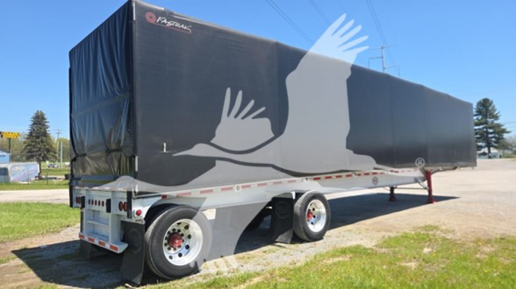 Curtainside trailer in-service showing black tarp with light gray graphic and white wheels under sunlit sky.