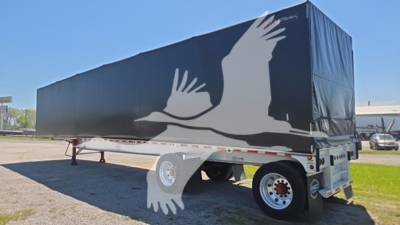 Trailer side view showing curtainside trailer with large white dove graphic on dark blue tarpaulin and rear bumper area.