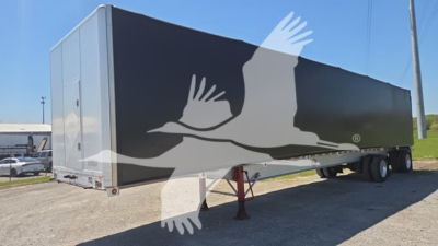 Trailer side view showing a large graphic of birds in flight on a dark gray curtain-side trailer with landing legs visible.