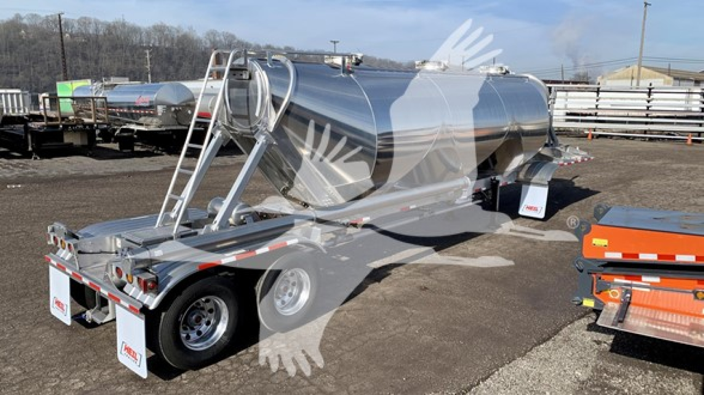 Trailer in a lot showing a polished stainless steel Heil cementer tanker with dual-axle wheels and rear riser, connected hoses, and safety mirrors.