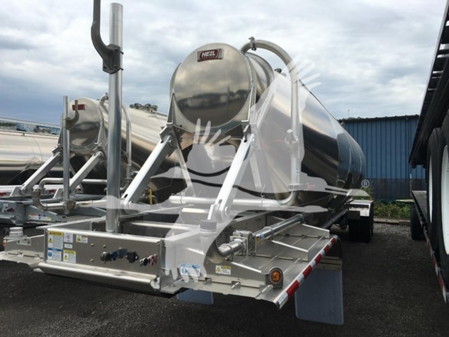 Heil cementer trailer with stainless steel tank and chrome frame, mounted dual axles, view from front-left showing control panel and piping.